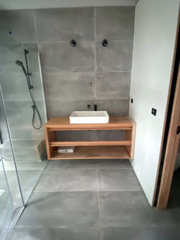 Baño con ducha, revestimientos grises y vanitorio de madera en etapa de terminaciones