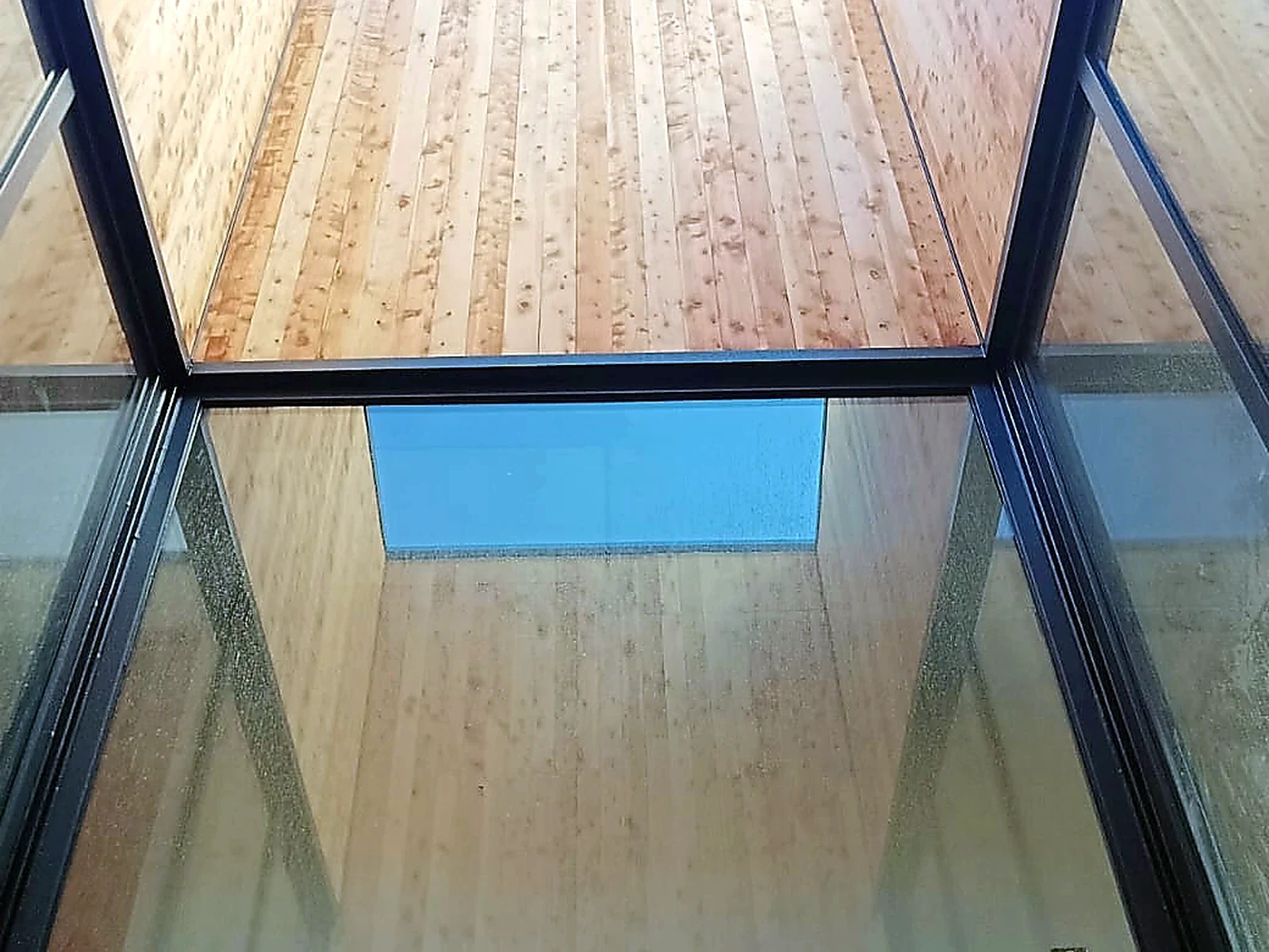 Detalle cenital de encuentro entre revestimiento de madera, vidrio y perfilería metálica oscura